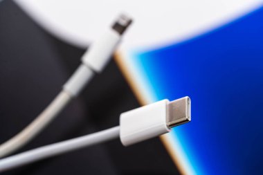 Beyaz USB-C erkek konnektörünü, arka planda odak dışı Şimşek erkek konnektörüyle kapat