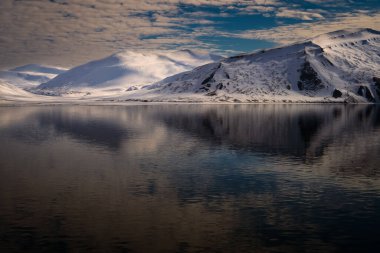 SVALBARD Norrway 'in yakınlarındaki okyanusta bulutlu bir gökyüzü ve bir yansıma ile kaplı kar dağları
