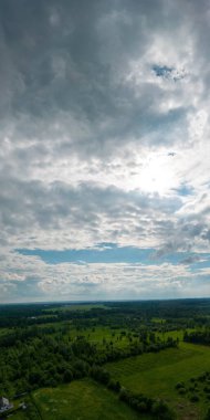 Bulutlu bir gökyüzüne karşı ağaçlarla ve tarlalarla çevrili dikey bir manzara.
