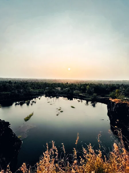 Gün batımında yemyeşil ağaçlarla çevrili küçük bir göl manzarası.