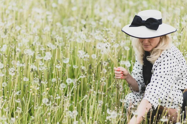 タンポポの畑で帽子をかぶっている美しいブロンドの女性 — ストック写真