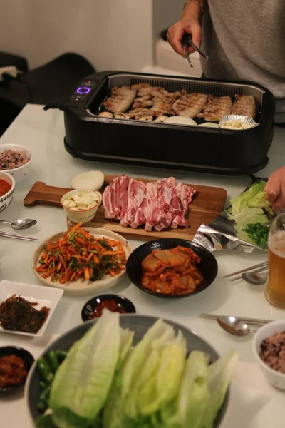 Kapalı ızgaralı bir yemek masasının dikey görüntüsü tahtada et, sebze tabakları.