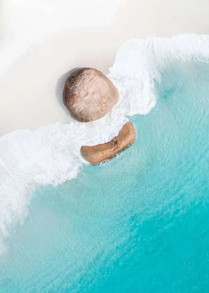 An aerial top view of waves washing an idyllic white sand beach with rocks in vertical