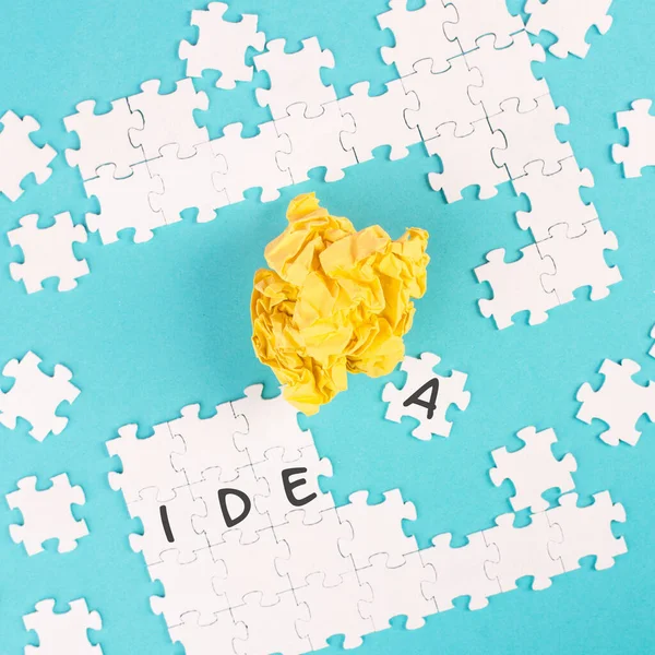Mavi bir arka planda bulmaca, sarı parçalanmış kağıt, kelime fikri yapboz parçaları üzerinde duruyor, beyin geliştirme konsepti, takım olarak çalışmak.