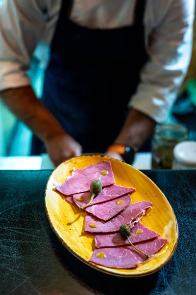 Sarı tabaktaki jambonun dikey çekimi, arka planda çalışan bir şef.