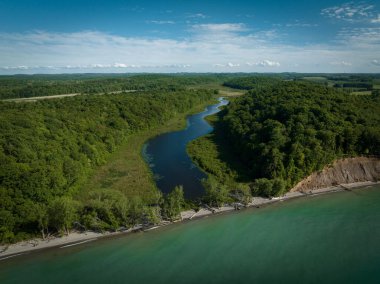 Bulutlu mavi gökyüzünün altında yeşil kıyılarından akan bir nehrin havadan görünüşü.