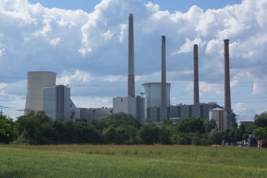 Almanya 'nın Hanau kenti yakınlarındaki Staudinger kömür yakıtlı enerji santrali, beyaz-mavi gökyüzüne karşı tarımsal bir arazide gömülü. Açık
