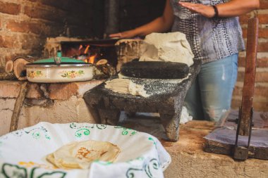 Meksika 'lı bir kadın tortilla yapmak için bir metastaz ve odun sobasında mısırlı sprey hazırlıyor.