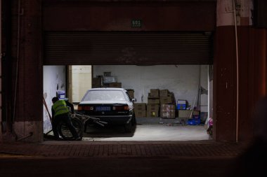 İşçi yeleği giymiş biri Şangay, Çin 'de arabasıyla garaja giriyor.