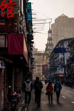 Arka planda binalarla Şangay sokaklarında yürüyen insanların dikey görüntüsü.