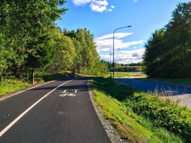 Gün boyunca yeşil ağaçlarla çevrili güzel bir yol görüntüsü.