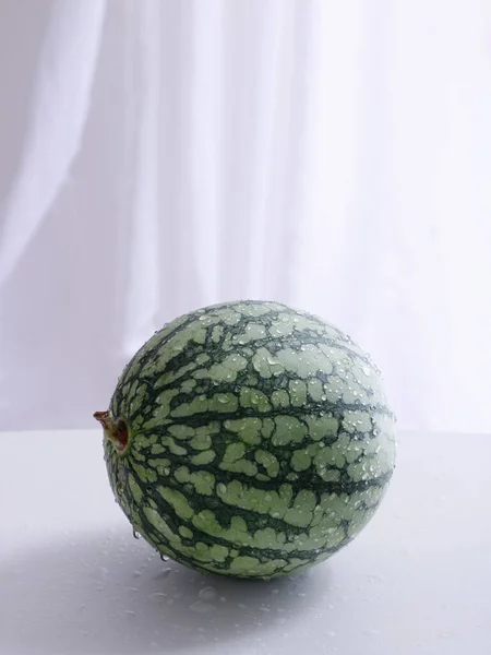 白色表面上的一个绿色小西瓜的垂直截图 — 图库照片