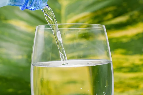 在模糊的绿色背景下 从瓶子中将清澈的饮用水倒入玻璃杯 — 图库照片
