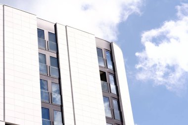 Mavi bulutlu gökyüzünün altındaki beyaz ve gri apartmanların modern cephelerinin düşük açılı bir görüntüsü.