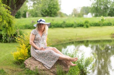 Beyaz bir kadın gölün kenarında oturuyor.