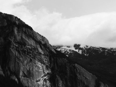Bulutlu bir gökyüzünün altındaki kayalıkların gri tonlu görüntüsü..
