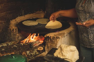 Meksika 'lı bir kadının mısır hamuru ile bir meta ve ahşap soba üzerinde çalışarak tortilla yapmasını izlemek.