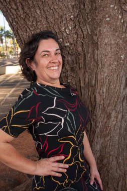 Güneşli bir günde parkta olgun bir bayan bir ağaca karşı durarak eğleniyor..