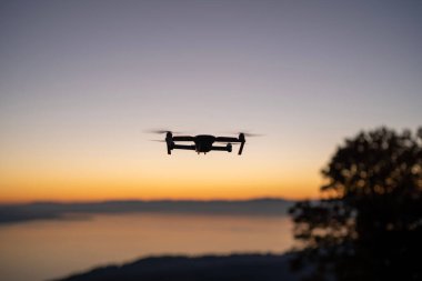 Gün batımında gökyüzünün arka planında süzülen dronun silueti. Vaud, İsviçre.