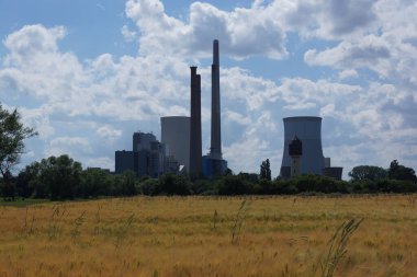 Almanya, Hanau yakınlarındaki Staudinger kömür santralinin silueti, bir tahıl tarlasının arkasında. Adım adım devre dışı bırakıldı. Mavi-beyaz gökyüzü.