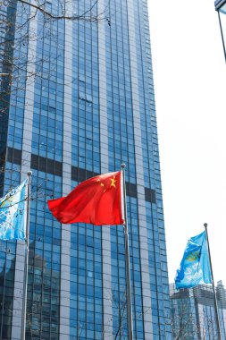 Çin bayrağının rüzgarda dalgalandığı dikey bir görüntü. Arka planda mavi bina, Şangay, Çin.