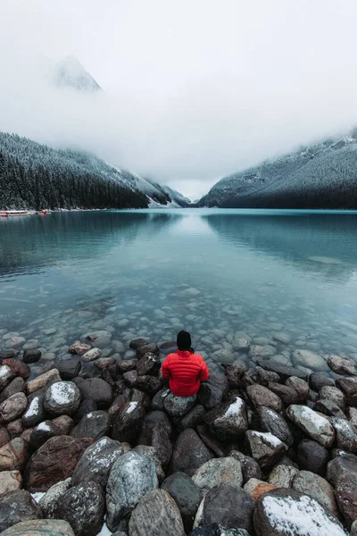 Vertical Shot Man Sitting Rocks Icy Lake Louise Snow Capped — Stock Photo, Image