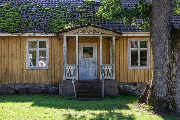 A view of the front entrance of an old wooden cottage with a mossy roof in the countryside