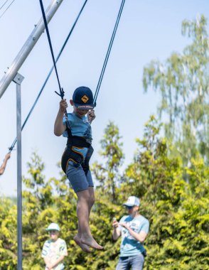 Poznan 'da bir parkta trambolinde güvenlik ekipmanıyla zıplayan bir çocuğun dikey görüntüsü.