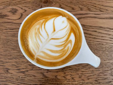 Ahşap arka planda latte sanatıyla dolu bir fincanın üst görüntüsü.