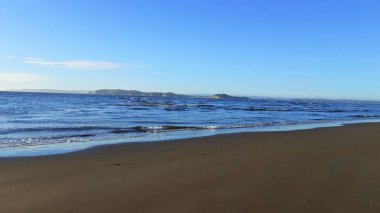 Güzel bir kumlu sahil manzarası ve mavi gökyüzünün altında sakin bir su.
