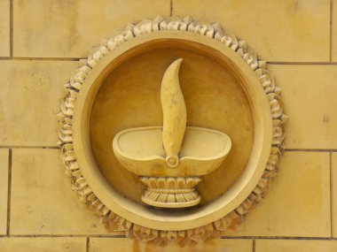 Sarı tuğla duvarda daire şeklinde çerçeveli meşale heykeli..