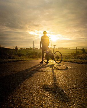 Bisikletin yanında oturan adam gün batımını izliyor..