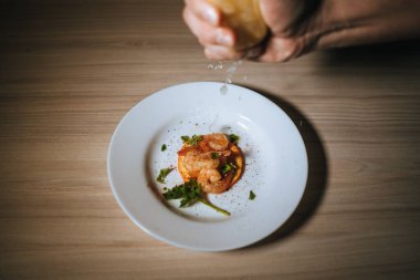 Bir şefin, taze otlarla dolu bir tabak karides tabağına limon sıkarkenki görüntüsü.