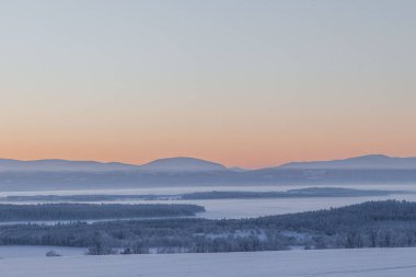 İsveç 'te gün batımında karla kaplı ormanlı sakin bir manzara.