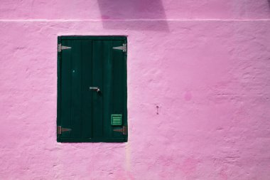 Pembe duvarında yeşil panjurlar olan bir pencere.