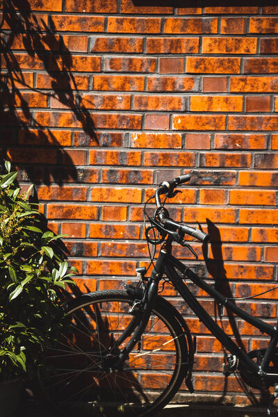A vertical shot of a black bicycle leaned on a brick wall in sunny weather