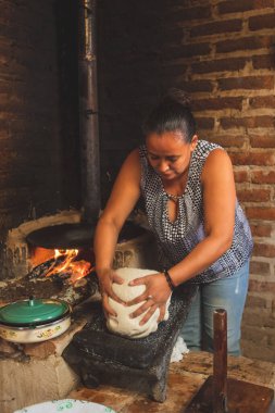 Meksikalı bir kadının dikey görüntüsü. Metate üzerinde mısırlı sprey ve tortilla yapmak için odun sobası hazırlıyor.