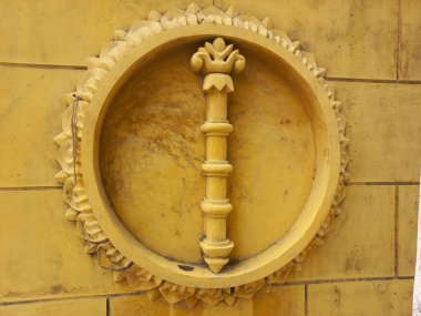 Sarı tuğla duvarda daire şeklinde çerçeveli asa heykeli..