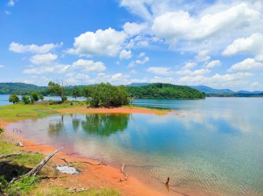 Huzurlu bir göl, tepeler ve arka planda kabarık bulutlarla güzel bir doğal manzara.