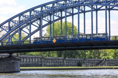 Bulutlu bir arka planda, kırsal bir alanda köprüden geçen bir trenin manzarası.