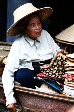 Taylandlı bir kadının Bangkok, Tayland 'da yüzen bir pazarda mal satarken çekilmiş dikey bir fotoğrafı.