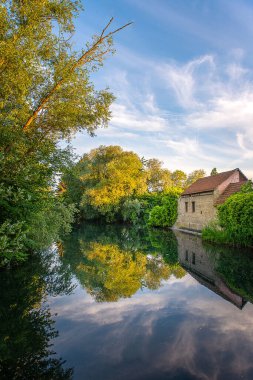 Bir ayna gölü ve sabah yeşil bir ormanda taş bir ev.