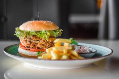 Lezzetli bir hamburger, patates kızartması ve tabakta salata.