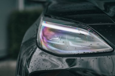 Yağmur damlalarıyla renkleri yansıtan bir arabanın farının yakın plan çekimi.