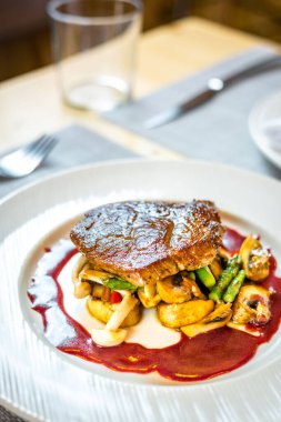 Beyaz bir tabakta ızgara sebze üzerinde bir bifteğin dikey görüntüsü.