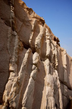 Çölde, parlak mavi bir gökyüzünün altında gölgeyle kaplı kayalık kahverengi uçurumların dikey görüntüsü.