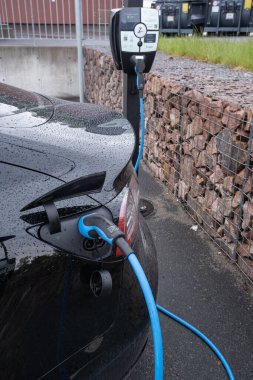 Yağmurlu bir bahar gününde Kople AC şarj istasyonuna siyah siyah bir Tesla Model 3 'ün statik görüntüsü.