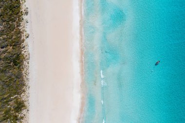 Gökyüzü kumlu bir plajın ve kristal berrak, deniz mavisi bir suyun hava aracı görüntüsü.