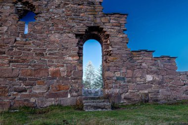 Eski bir taş binanın harabelerinde mavi gökyüzü arka planına karşı bir kemer girişi.