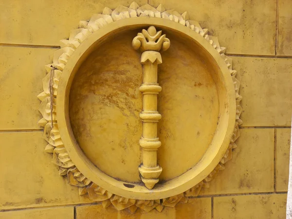 Sarı tuğla duvarda daire şeklinde çerçeveli asa heykeli..